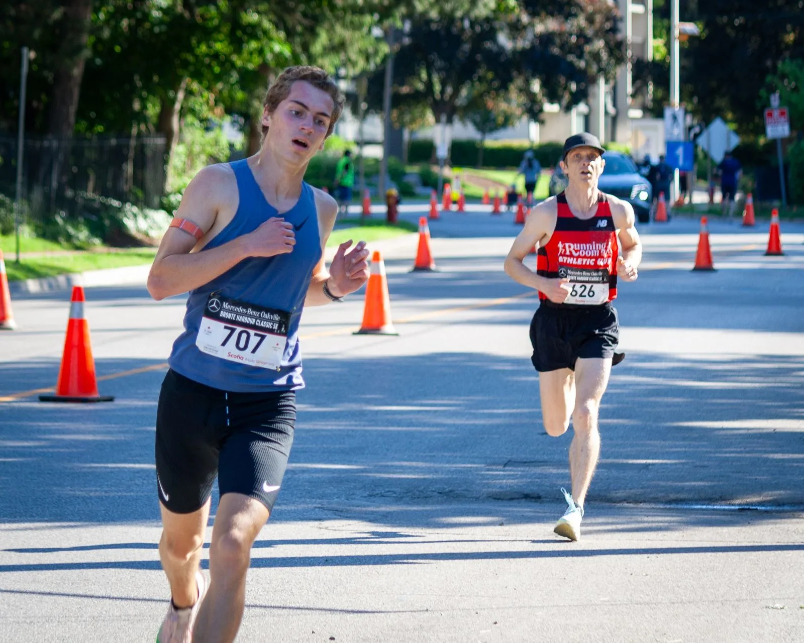 Two lead runners with clearly visible bib numbers 707 and 626 racing along the tree-lined Bronte Harbour Classic 5K course, Oakville